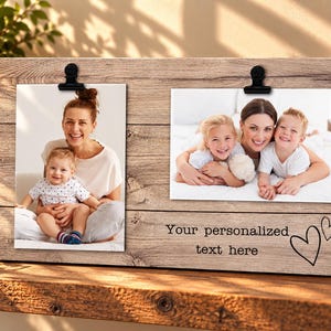 May include: A rectangular wooden photo display board with a light brown wood grain finish. It features two black metal clips at the top to hold photographs. The board includes the printed text "Your personalized text here" and two heart outlines.