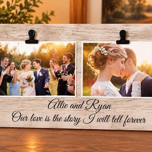 May include: A rectangular light wood-grain photo frame featuring two black metal clips to hold photographs. The frame is printed with the text "Allie and Ryan" and "Our love is the story I will tell forever" in a black cursive script font.