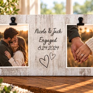 May include: A rectangular light-colored wood photo display board featuring two black metal clips holding photographs. The center text reads Nicole & Jack Engaged 8.24.2024, accompanied by two hand-drawn heart outlines. The board has a weathered finish.