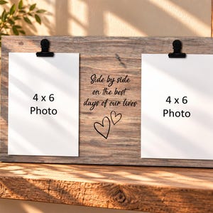 May include: A rectangular wooden photo display board with a weathered brown finish. It features two black metal clips holding white 4x6 photo placeholders. The center text reads Side by side on the best days of our lives with two heart outlines.