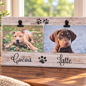 Può includere: Una cornice portafoto rettangolare in legno con finitura effetto venatura del legno marrone chiaro. Presenta due clip in metallo nero nella parte superiore per fissare le foto. La cornice riporta la scritta nera "Cocoa" e "Latte" con due impronte.