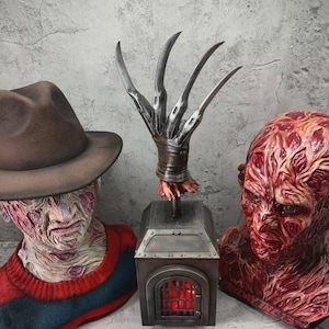 Puede incluir: Un conjunto que incluye un busto de una figura con cicatrices, un sombrero fedora marrón y un suéter rojo y azul, un guante metálico central con cuatro hojas largas sobre una caja con rejilla roja, y otro busto con el texto Friday the 13th.