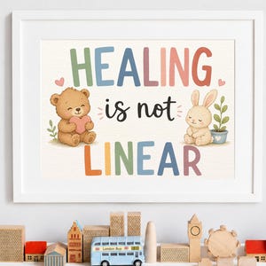 May include: A white framed wall art print featuring the text HEALING is not LINEAR in colorful letters. The illustration includes a brown teddy bear holding a pink heart and a beige rabbit sitting next to a small potted green plant.