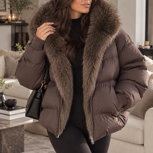 May include: A dark brown puffer jacket featuring a large, plush faux fur collar, long sleeves with ribbed cuffs, and a front zipper closure. The jacket has a quilted design and is worn over a black top and black leggings, paired with a black handbag.