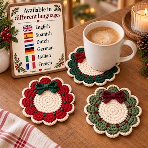 Puede incluir: Tres posavasos redondos de ganchillo con bordes festoneados, con un centro color crema, un anillo exterior rojo o verde y un pequeño lazo a juego. Un posavasos sostiene una taza de cerámica blanca con café junto a un cartel informativo.