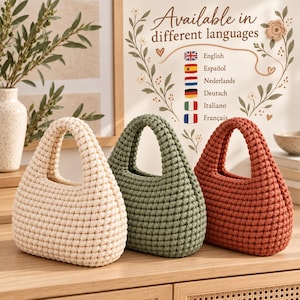 Può includere: Tre piccole borse arrotondate realizzate in corda spessa annodata nei colori crema, verde salvia e terracotta. Ogni borsa presenta un manico integrato e una superficie intrecciata testurizzata. Un cartello dietro riporta Available in different languages.