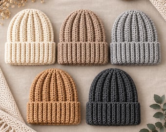 Pode incluir: Cinco gorros de malha dispostos em duas filas, com textura canelada e barra dobrada. As cores incluem creme, castanho claro, cinzento claro, castanho médio e cinzento carvão escuro. Cada gorro apresenta um padrão de ponto vertical consistente.
