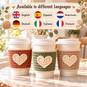 May include: Three white disposable coffee cups featuring textured crochet sleeves in rust, sage green, and beige. Each sleeve displays a cream-coloured crocheted heart. Above the cups, a sign reads Available in different languages with flags.