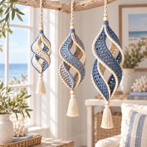 May include: Three hanging spiral ornaments crafted from blue and cream-colored crochet yarn. Each piece features a twisted open-work design, a wooden bead at the top and bottom, and a cream-colored tassel hanging from the base of each ornament.