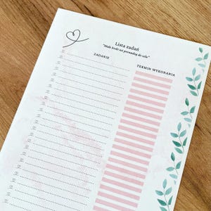 Op de afbeelding: Een wit takenlijstblad met de tekst Lista zadań en Małe kroki też prowadzą do celu. De pagina bevat een kolom voor taken met kleine hartjes en een kolom voor deadlines met roze horizontale balken, geaccentueerd door groene bladeren.
