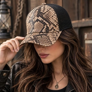Può includere: Un cappellino da baseball con un motivo a pelle di serpente beige e nero sui pannelli frontali e sulla visiera, completato da una rete posteriore nera. Il cappellino presenta una corona strutturata, una visiera curva e un bottone centrale.