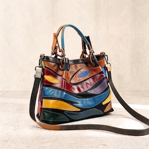 Puede incluir: Un bolso de mano multicolor con un diseño de parches de cuero en tonos marrón, negro, rojo, azul, amarillo, verde y morado. El bolso incluye dos asas superiores, una correa de hombro oscura desmontable y herrajes de color plateado.