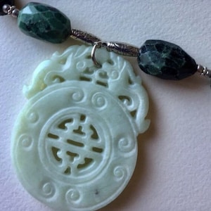 May include: A jade green pendant necklace with a carved jade pendant featuring a Chinese knot design. The pendant is attached to a silver chain with green and silver beads.