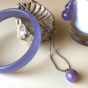 May include: A set of lavender jade jewelry featuring a bangle bracelet, a pendant necklace, and a pair of earrings. The pendant and earrings are shaped like gourds.