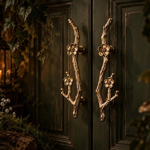 May include: A pair of vertical door handles crafted from brass with a textured, branch-like finish. Each handle features two prominent floral blossoms integrated into the stem, providing a decorative grip for double doors with a metallic gold tone.