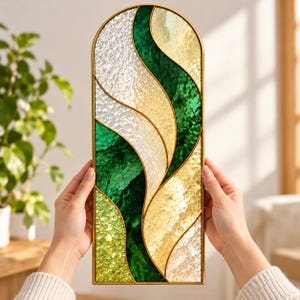 May include: An arched wall panel featuring a mosaic design with curved sections of textured glass in shades of emerald green, lime green, cream, and white, all encased within a thin gold-colored metal frame with a smooth, rounded top edge.