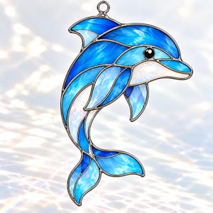 以下が含まれることがあります： 青色と虹色の白色のガラス片を暗い金属のハンダでつなぎ合わせた、イルカの形をしたステンドグラスのサンキャッチャー。イルカは跳ねるようなポーズで描かれており、上部には吊り下げるための小さな金属製のリングが付いています。