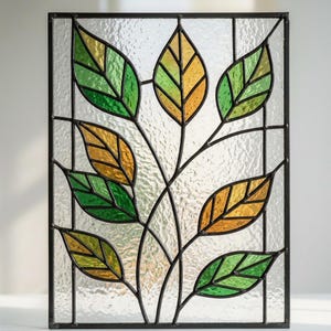 May include: A rectangular stained glass panel featuring a black metal frame and a central branch design with multiple leaves. The leaves are crafted from textured green and amber glass, while the background consists of clear, rippled glass.