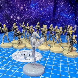 May include: A collection of tan-colored droid figurines standing on circular bases. Most are painted with black blasters, while one unpainted, translucent gray droid stands in the foreground. The figures feature thin, robotic limbs and heads.
