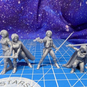 May include: Four unpainted grey resin miniature figures in dynamic action poses. Three figures stand while one kneels, all wearing tactical gear, capes, and hoods. They hold long, thin rod-like weapons, and one figure holds a small blaster pistol.