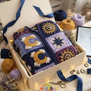 May include: A crochet cardigan made of square motifs featuring yellow suns, moons, and stars on dark blue and purple backgrounds, packed in a gift box with yarn balls, a gold crochet hook, metal charms, scissors, and stitch markers.