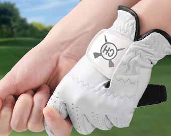 May include: A white golf glove with black trim and perforated detailing on the fingers. The glove features a prominent white velcro closure tab on the back of the hand, displaying a circular logo with the letters CH and a cross design.