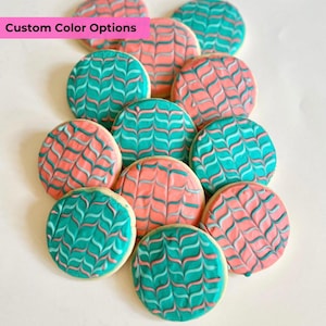 May include: A collection of round sugar cookies decorated with a teal and pink swirl pattern. The cookies are arranged in a pile on a white surface. The text "Custom Color Options" is displayed in a pink banner at the top of the image.