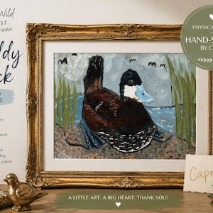 Può includere: Una stampa artistica incorniciata intitolata Ruddy Duck che raffigura un'anatra marrone con il becco blu seduta su una riva di ciottoli vicino all'acqua e canne verdi. La stampa misura 20x25 cm e include la firma autografa di Capri.