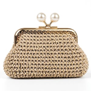 May include: A beige crochet clutch bag featuring a gold-toned metal frame with a scalloped edge. The clasp is secured by two round, white faux pearl beads. The body of the bag is constructed from a textured, woven yarn with subtle metallic gold flecks.
