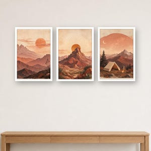 Op de afbeelding: Een set van drie rechthoekige wandkunstprints met woestijn- en berglandschappen in tinten terracotta, oranje en beige. De afbeeldingen tonen gelaagde bergketens, een zon met stralende lijnen en een kampeerplek met een tent en een kampvuur.