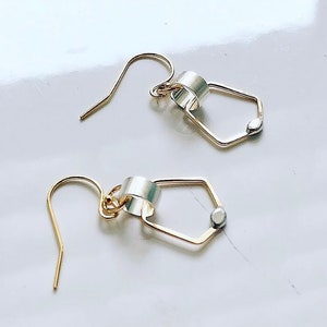 May include: A pair of gold earrings with a silver ring and a small silver bead. The earrings are in the shape of a hexagon.