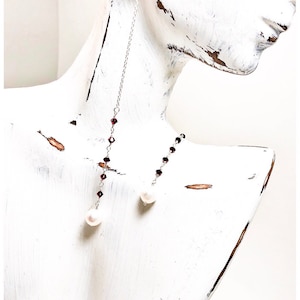 May include: A pair of long silver chain earrings with burgundy crystal beads and a white pearl at the end of each chain.