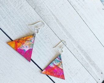 May include: A pair of triangle-shaped earrings with a colorful abstract design. The earrings are made of wood and have silver hooks.