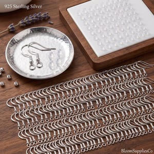 May include: A large collection of 925 sterling silver earring hooks with a coiled spring and loop design. The set includes clear silicone earring backs arranged on a white square tray and a small hammered silver dish containing two hooks.