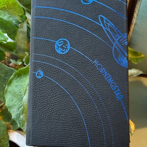 May include: Black book with blue celestial design. The cover features a textured surface with a blue illustration of planets and orbital lines. The word "MORNINGSTAR" is printed in blue.