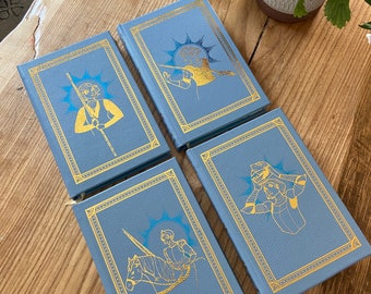 May include: Four blue hardcover books with gold accents and illustrations. Each book features a different image of a person in a fantasy setting.