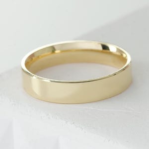 Peut inclure: Une bague anneau en or poli avec une surface lisse et plate, présentant un design circulaire simple et continu. La bague possède une finition métallique réfléchissante et une largeur uniforme, offrant une esthétique épurée sans gravures.