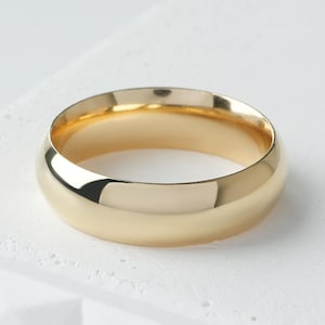 May include: A polished gold band ring with a smooth, rounded exterior surface and a high-shine finish. The ring features a simple, solid construction with a consistent width throughout, showcasing a reflective metallic yellow gold tone.