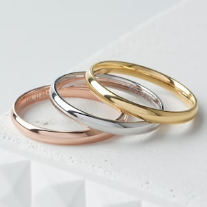 Peut inclure: Un ensemble de trois bagues en métal lisse et poli, déclinées dans des tons or rose, argent et or jaune. Chaque bague présente un design simple à anneau arrondi avec une finition brillante, empilées en léger chevauchement.
