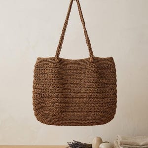 May include: A brown woven tote bag with a rectangular shape and two matching shoulder straps. The bag features a textured, horizontal ribbed pattern throughout its body, constructed from a natural-looking fiber material in a warm, earthy tone.