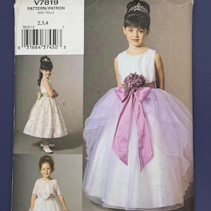 May include: Vogue for Me sewing pattern V7819. The pattern features three different styles of girls' dresses. The main image shows a young girl in a white dress with a pink sash and bow. The pattern includes sizes 2, 3, and 4.