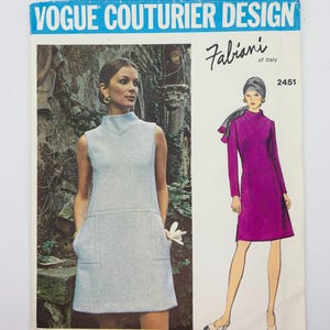 May include: A vintage Vogue Couturier Design sewing pattern featuring a Fabiani of Italy design. The pattern includes illustrations of two dresses: a sleeveless light blue dress and a long-sleeved magenta dress. The pattern number is 2451.