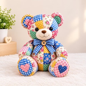 Peut inclure: Un ours en peluche en patchwork composé de divers carrés de tissu à motifs vichy bleu, pois jaunes et fleurs roses. L'ours possède un nez marron, des yeux noirs, un nœud papillon vichy bleu avec un bouton en bois et des patchs en forme de cœur.
