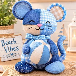 Può includere: Un peluche a forma di topo realizzato con vari tessuti blu e bianchi, tra cui denim, quadretti vichy e motivi a pois. Il topo presenta un naso rosa ricamato, un fiocco a quadretti blu al collo e tiene in mano una palla a righe blu e bianche.