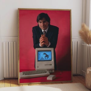 May include: A framed portrait print featuring a person in a dark suit and tie standing behind a vintage beige desktop computer with a keyboard and mouse. The background is a solid red colour. The computer screen displays a black and white graphic.