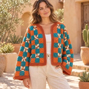 May include: A long-sleeved crochet cardigan featuring a checkerboard pattern of alternating burnt orange and teal square motifs. The garment has an open front design with a solid orange crocheted border along the edges and wide sleeves.