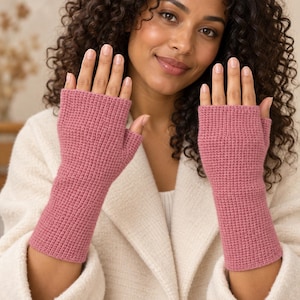 Könnte beinhalten: Ein Paar fingerlose Handschuhe in Altrosa mit einem strukturierten, gitterartigen Strickmuster. Die Handschuhe reichen von den Knöcheln bis zur Mitte des Unterarms und lassen die Finger und Daumen für mehr Beweglichkeit frei.