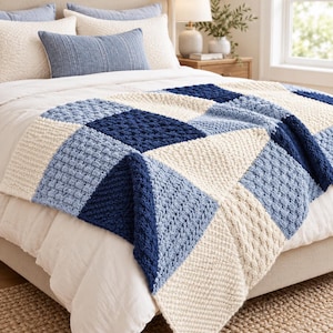 Könnte beinhalten: Eine grob gestrickte Wohndecke mit geometrischem Patchwork-Design in Marineblau, Hellblau und Creme. Die Decke besteht aus quadratischen Blöcken mit verschiedenen strukturierten Strickmustern und liegt auf einem Bett mit weißer Bettwäsche.