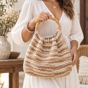 Puede incluir: Un bolso de ganchillo con rayas horizontales en tonos beige, marrón claro y crema. El bolso tiene una silueta redondeada y está rematado con dos asas circulares de bambú que ofrecen un contraste estructurado con el cuerpo de hilo texturizado.