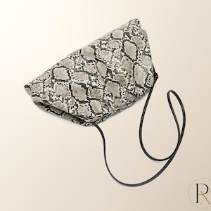 May include: A soft, gathered clutch bag featuring a grey, black, and white snakeskin pattern. The bag has a rounded, voluminous shape and includes a thin, black cord shoulder strap that hangs down from the side of the main body of the bag.